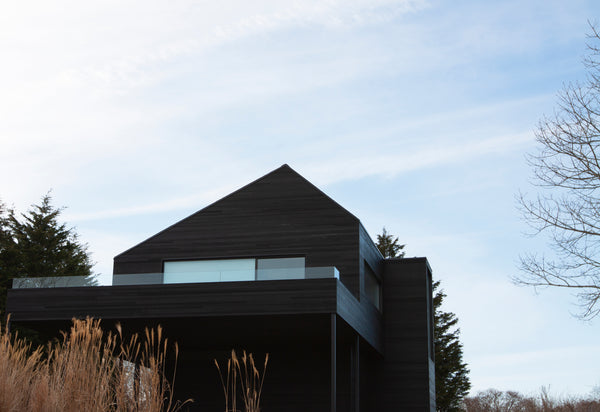 Montauk Beach House No.2 and it's black cedar siding with a pointed roof among clear blue skys and a winter landscape