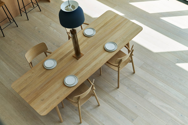 Overhead view of an oak dining table and four dining chairs by Skagerak with respective white ceramic plates