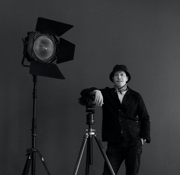 A black and white portrait of Jonathan Hökklo leaning on camera gear