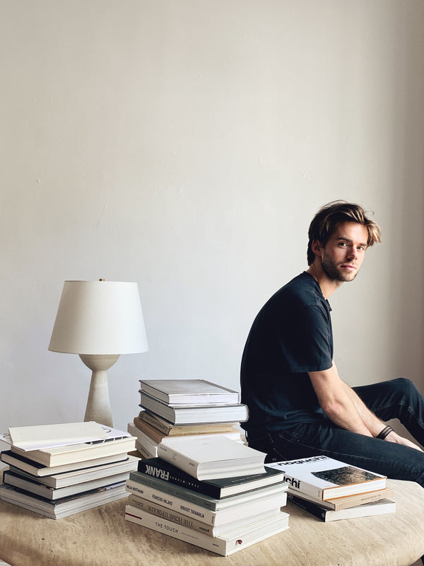 Colin King sits with a stack of books has a faces sideways towards the camera