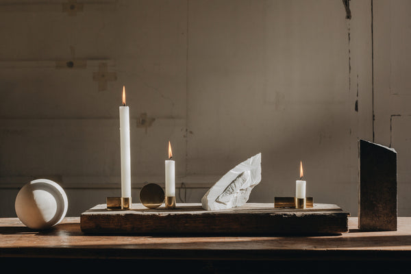 A table of small objet and three candle lit candles of staggering heights with a slight afternoon light shadow casting. 