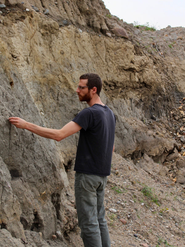 Mitch Iburg reaching out to pick a piece of wild clay from a side of a cliff or a foot of a mountain
