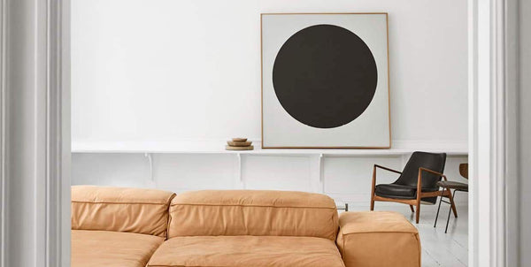 Ricky Nordson's living room with a sand/orange colored sofa, a painting of a large black dot with white background on the wall and a black midcentury modern chair next to it