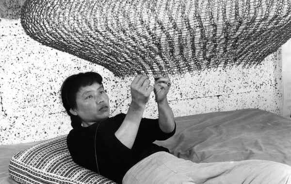 Ruth Asawa lying down on her back finishing up her wired sculptures